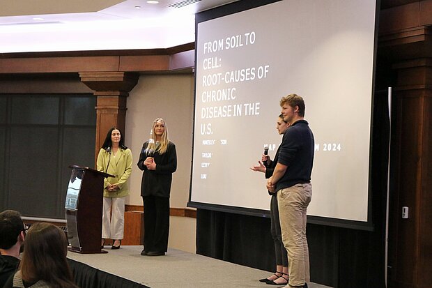 Photo of students standing in front of a screen as they present their Map the System project on the approach to diet-related disease in the U.S.