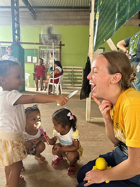 Photo of NDSU student with 3 small children who are fascinated with penlight used in exams in village clinic in Amazonas, Brazil.